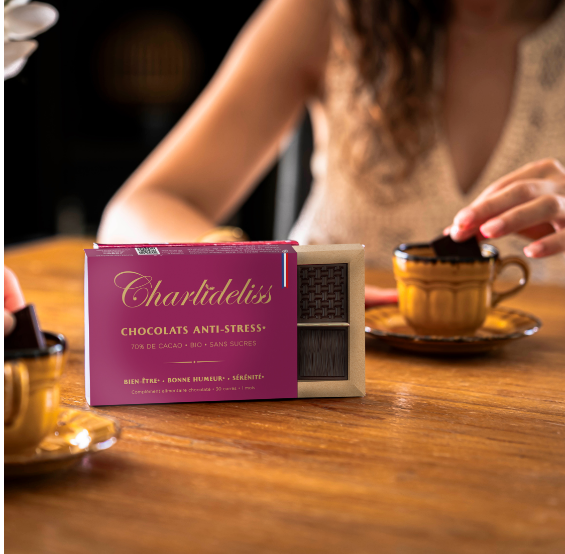 Chocolat^s anti-stress CHarlidéliss dans leur boîte, devant une femme qui trempe un carreau dans son thé