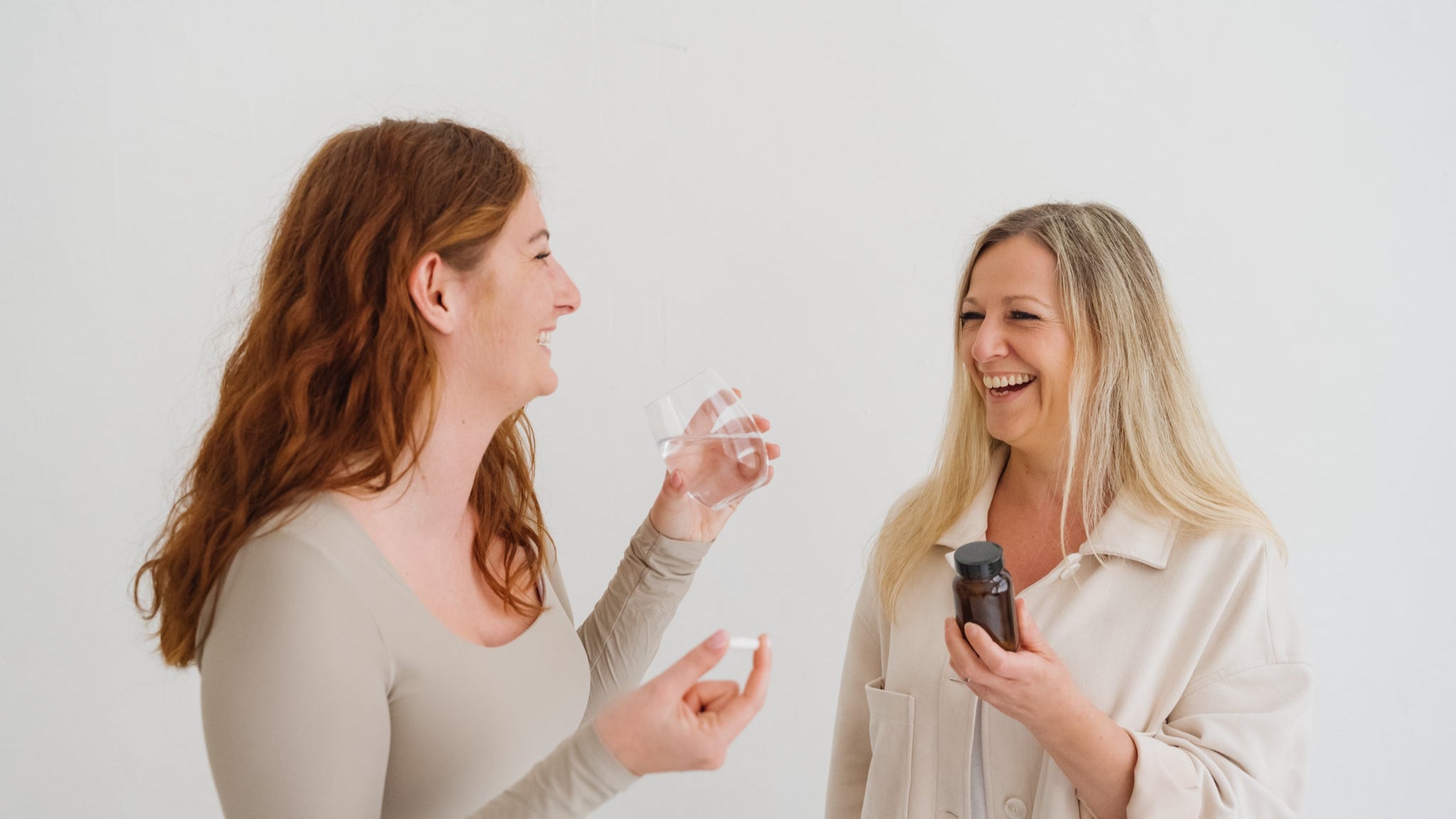 Deux femmes souriantes, l’une avec une gélule et un verre d’eau, l’autre avec un flacon de compléments